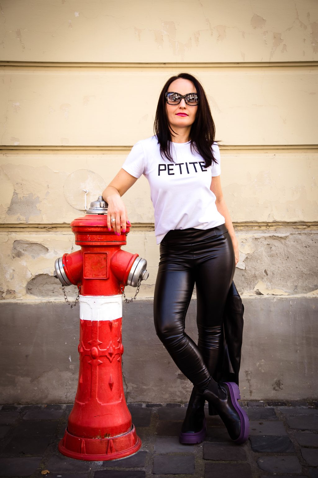 Nő fehér PETITE feliratú pólóban és bőrnadrágban egy utcai fotón